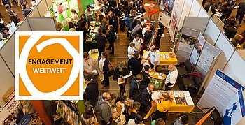 Im Hintergrund Messestände und Menschen. Im Vordergrund ist ein orangefarbenes Logo mit der Aufschrift 'Engagement weltweit' prominent platziert.