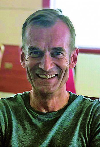 Ein lächelnder Mann in einem grünen Shirt, der vor einem roten Hintergrund sitzt.