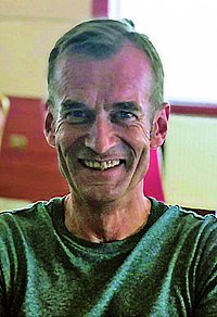 Ein lächelnder Mann in einem grünen Shirt, der vor einem roten Hintergrund sitzt.