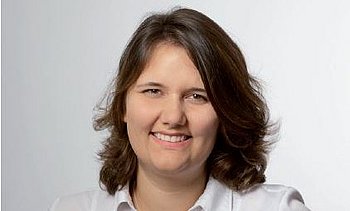 Porträt einer lächelnden Frau mit schulterlangem Haar vor einem neutralen Hintergrund.