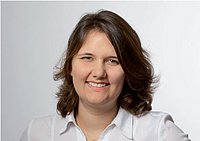 Porträt einer lächelnden Frau mit schulterlangem Haar vor einem neutralen Hintergrund.