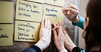 Personen, die bei einer Workshop-Diskussion Notizen an ein Whiteboard heften.