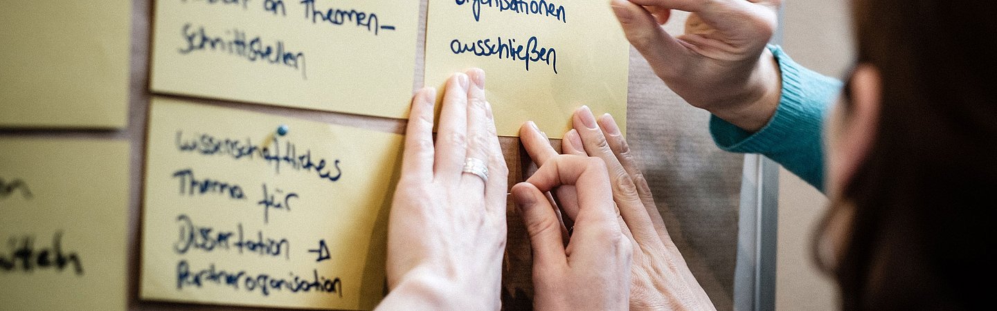 Personen, die bei einer Workshop-Diskussion Notizen an ein Whiteboard heften.