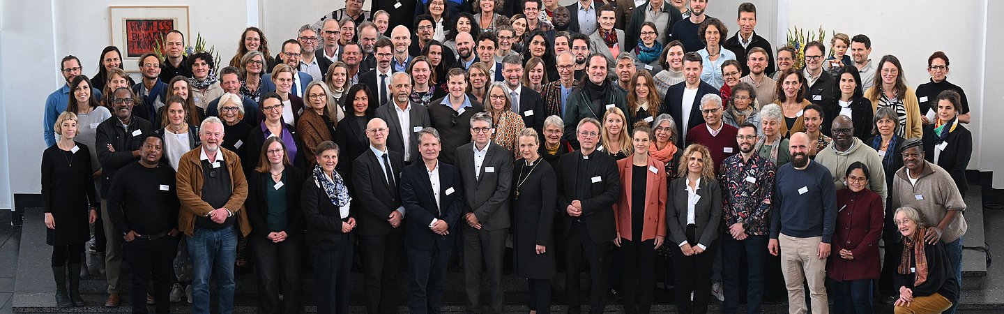 Ein großes Gruppenfoto, aufgenommen in einer Aula oder einem Konferenzraum, mit mehreren Reihen von Personen.