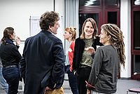 Eine Gruppe von Menschen steht zusammen und unterhält sich in einem Konferenzraum. Die Szene wirkt kommunikativ und dynamisch.