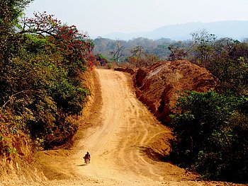 Eine unbefestigte, orangefarbene Straße schlängelt sich durch eine hügelige Landschaft.