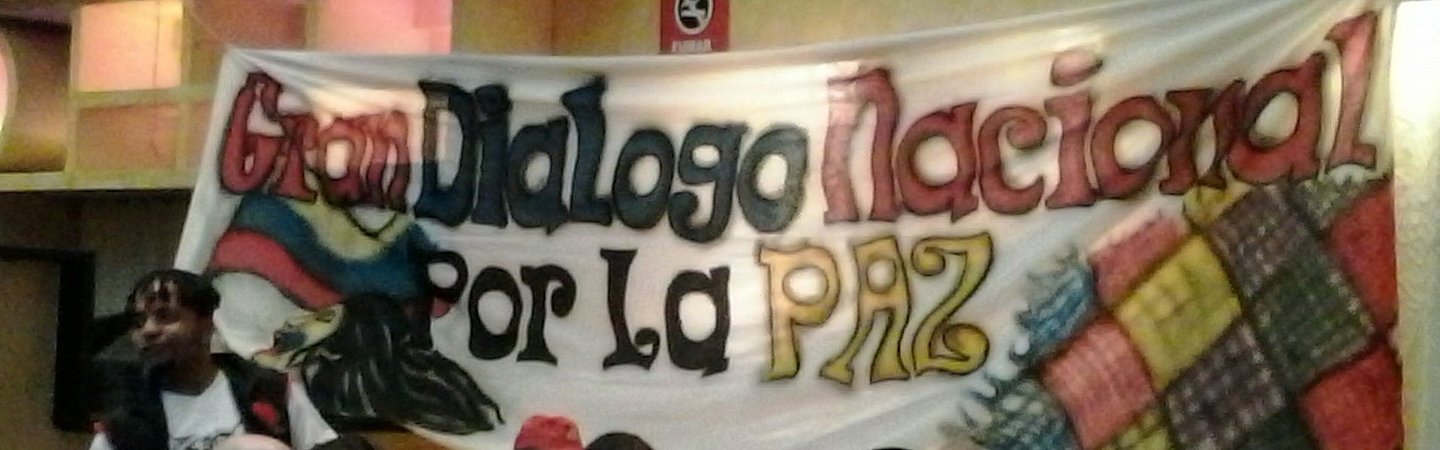 Eine Versammlung von Menschen in einem Saal, im Hintergrund ein großes Banner mit der Aufschrift „Dialogo Nacional por la Paz“ in lebendigen Farben.