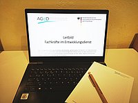 Ein Laptop auf einem Schreibtisch mit einem geöffneten Leitfaden für entwicklungspolitische Arbeit.