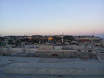 Panoramabild einer weitläufigen Landschaft mit Gebäuden und Strommasten, aufgenommen während der Dämmerung.