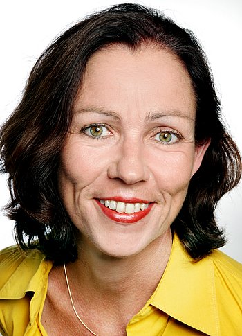 Portrait von Gabi Waibel. Eine Frau mit braunen schulterlangen Haaren und einer gelben Bluse, die in die Kamera lächelt. 