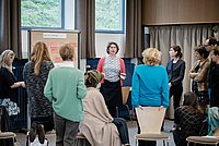 Teilnehmer eines Workshops stehen in einem Raum und tauschen sich aktiv aus. Die Atmosphäre wirkt offen und kollaborativ.
