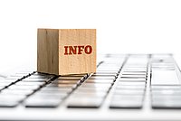 Ein Holzblock mit der Aufschrift „INFO“, der auf einer Tastatur liegt und auf Informationen hinweist.
