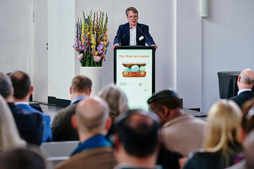Eine Person hält einen Vortrag an einem Rednerpult vor einem Publikum in einem Konferenzraum.