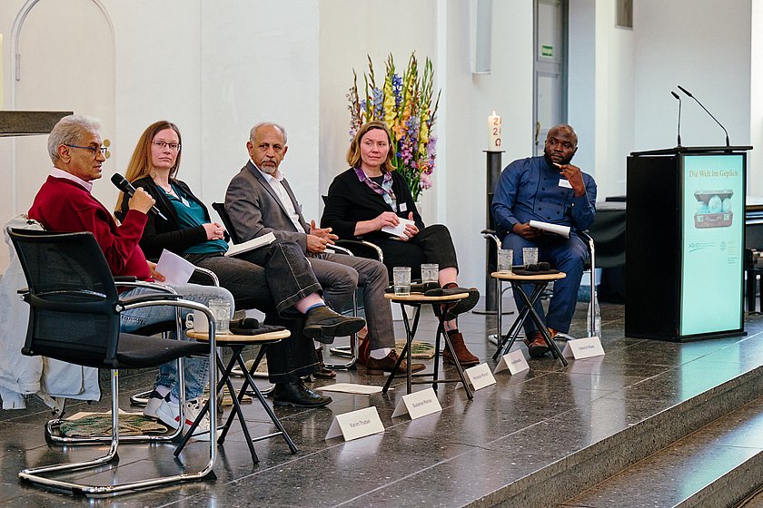 Eine Podiumsdiskussion mit mehreren Teilnehmern in einem großen, hellen Raum, mit Blumenarrangements im Hintergrund.