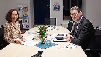 Zwei Personen, Gabi Waibel und Thorsten Schäfer-Gümbel bei einer Besprechung an einem Konferenztisch mit Blumen.