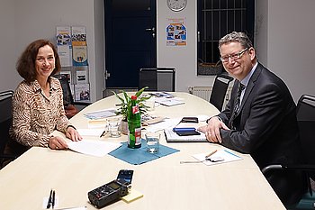 Zwei Personen, Gabi Waibel und Thorsten Schäfer-Gümbel bei einer Besprechung an einem Konferenztisch mit Blumen.