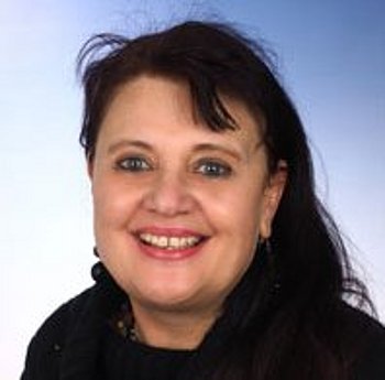 Porträt einer Frau mit dunklen, langen Haaren, die in die Kamera lächelt. Sie trägt einen schwarzen Schal und hat einen hellen Hintergrund.