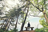 Person, die auf einer Bank in einem sonnendurchfluteten Wald sitzt und die Natur genießt.