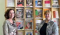 Eine Frau steht vor einem Bücherregal, das mit diversen Publikationen gefüllt ist.