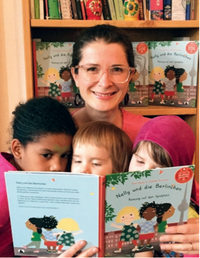 Eine Frau sitzt mit einem Kind, beide halten Kinderbücher in den Händen und lächeln.